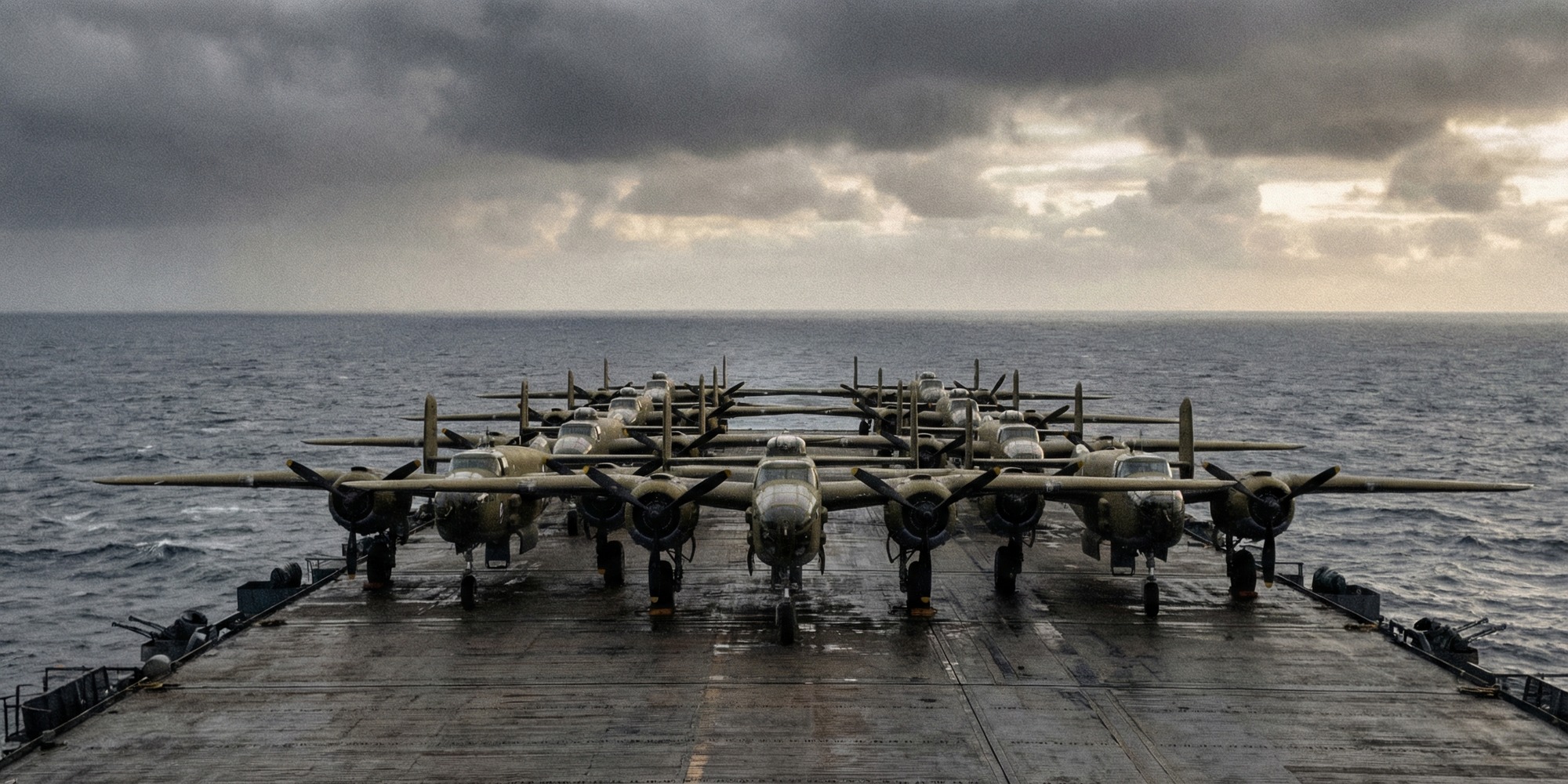 B-25 Mitchell bombers lined up on a carrier flight deck looking toward open ocean under an overcast wartime sky